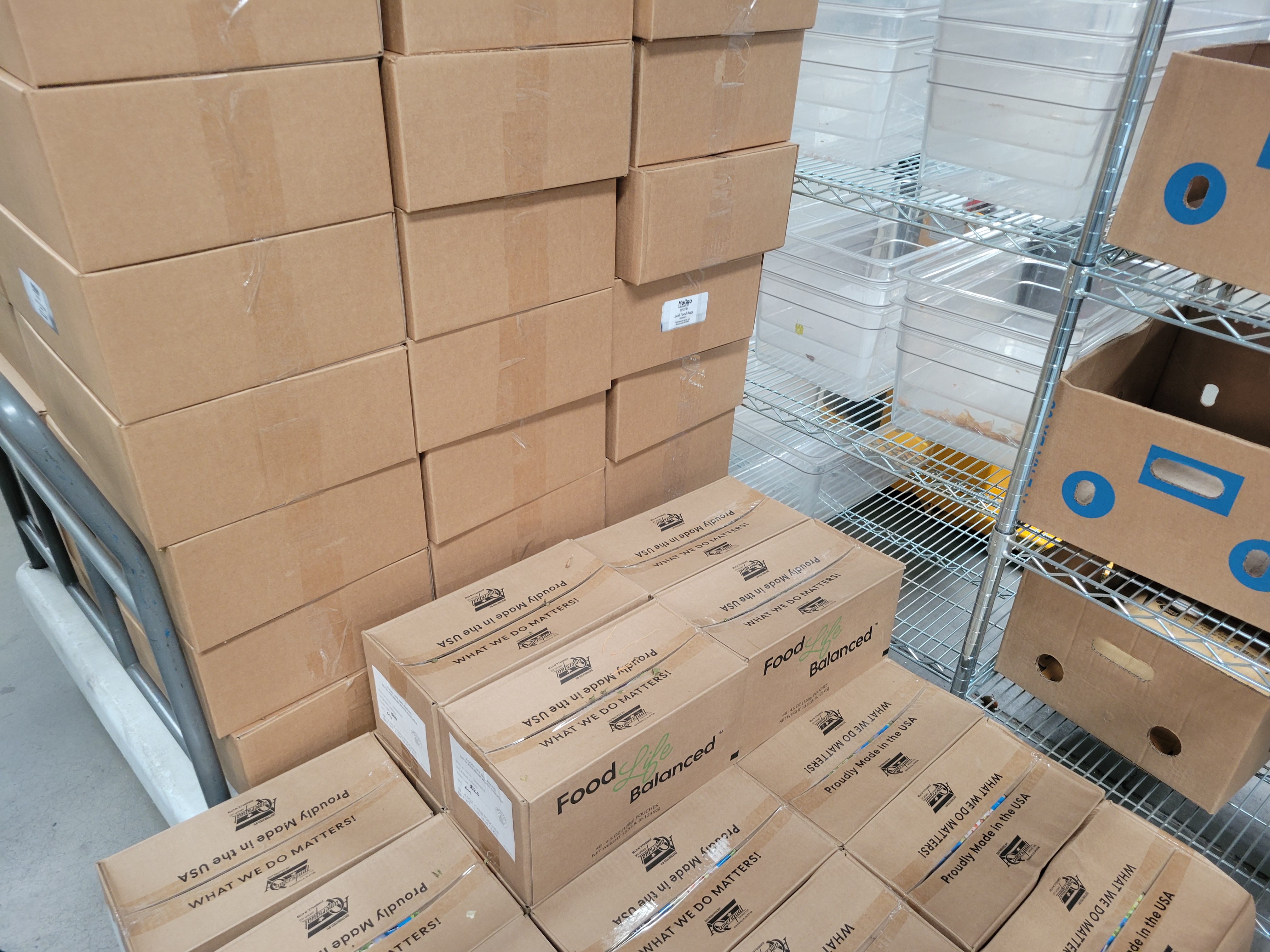Pallet of chicken and produce boxes on truck cart next to shelves filled with plastic containers and banana boxes.